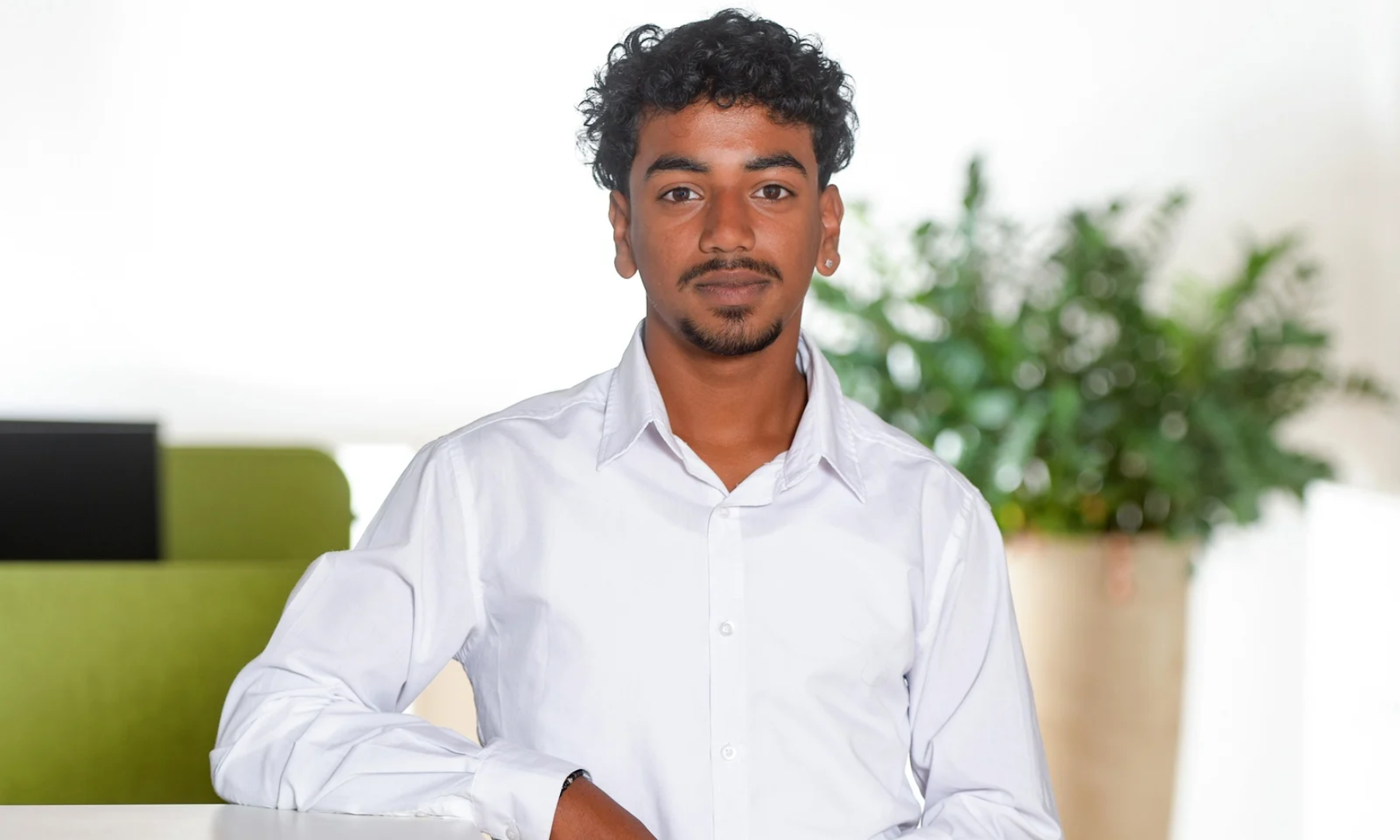 Nelo, sitting at a desk in an office, looking at the camera